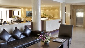 Eine großzügige Lobby mit modernem Design, inklusive einer Sitzecke mit einer Couch und Sesseln, einem zentralen Couchtisch und einer Rezeption.