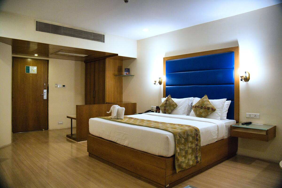 Habitación de hotel con una cama grande, cabecero de madera, mesitas de noche y una estantería empotrada.
