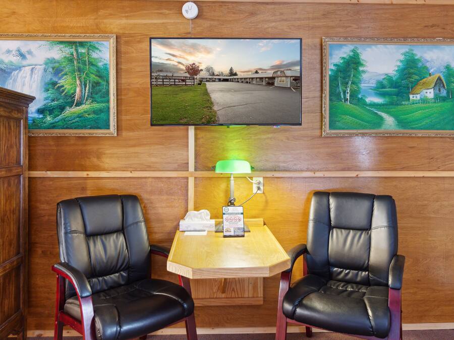Une pièce comprenant deux fauteuils en cuir, une table en bois, un téléviseur fixé au mur et des tableaux encadrés.