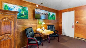 A room with a wooden wall, a desk, two chairs, a television, and a door.