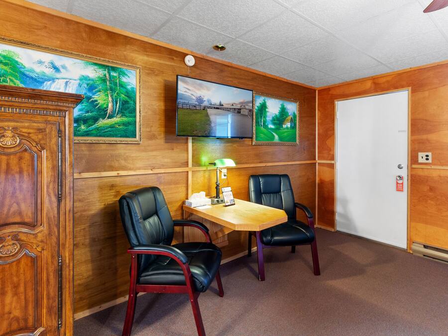 A room with a wooden wall, a desk, two chairs, a television, and a door.