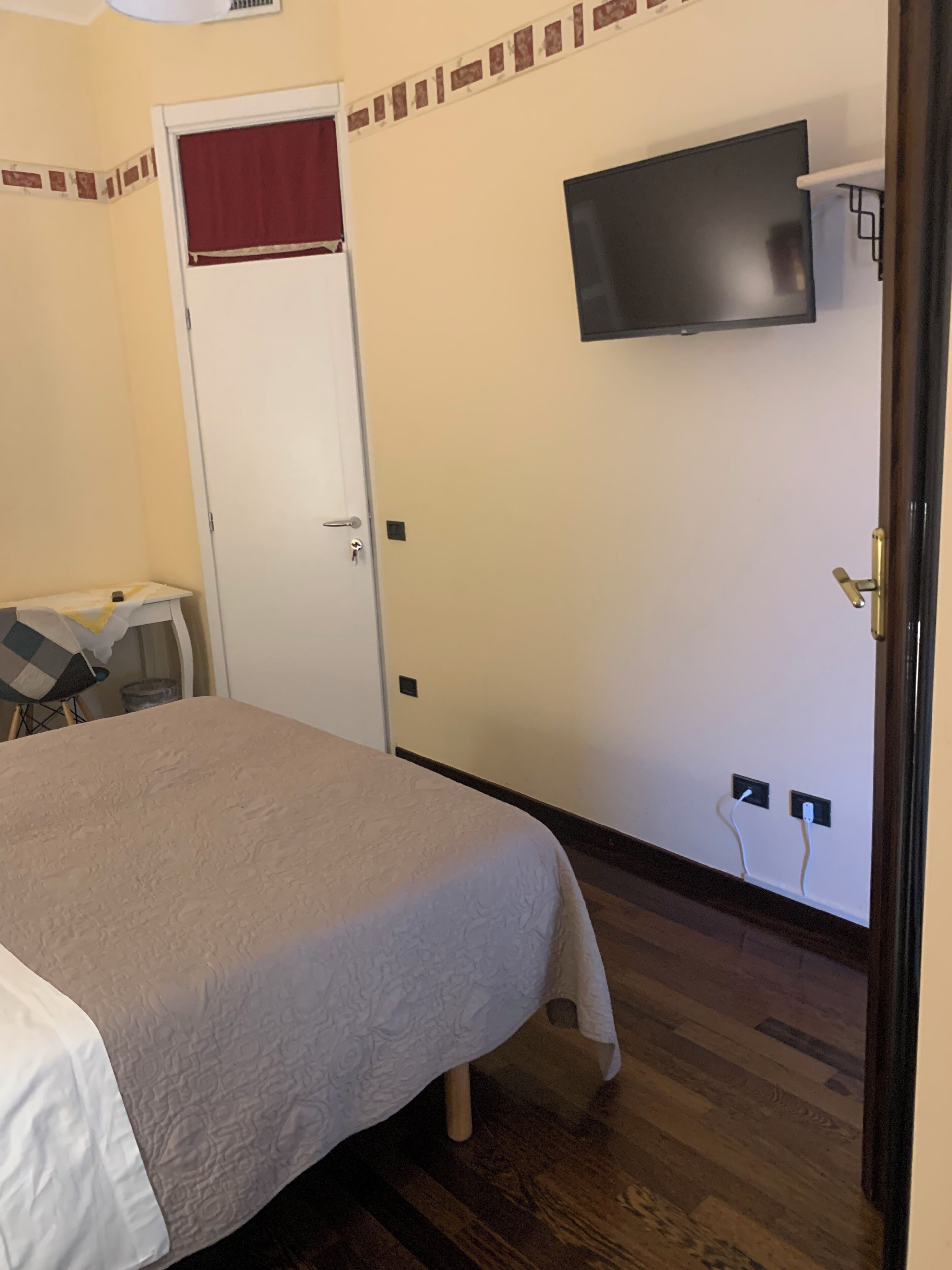 Ein Schlafzimmer mit einem Bett, einem an der Wand montierten Fernseher, einer Tür und einem kleinen Tisch mit Stuhl.