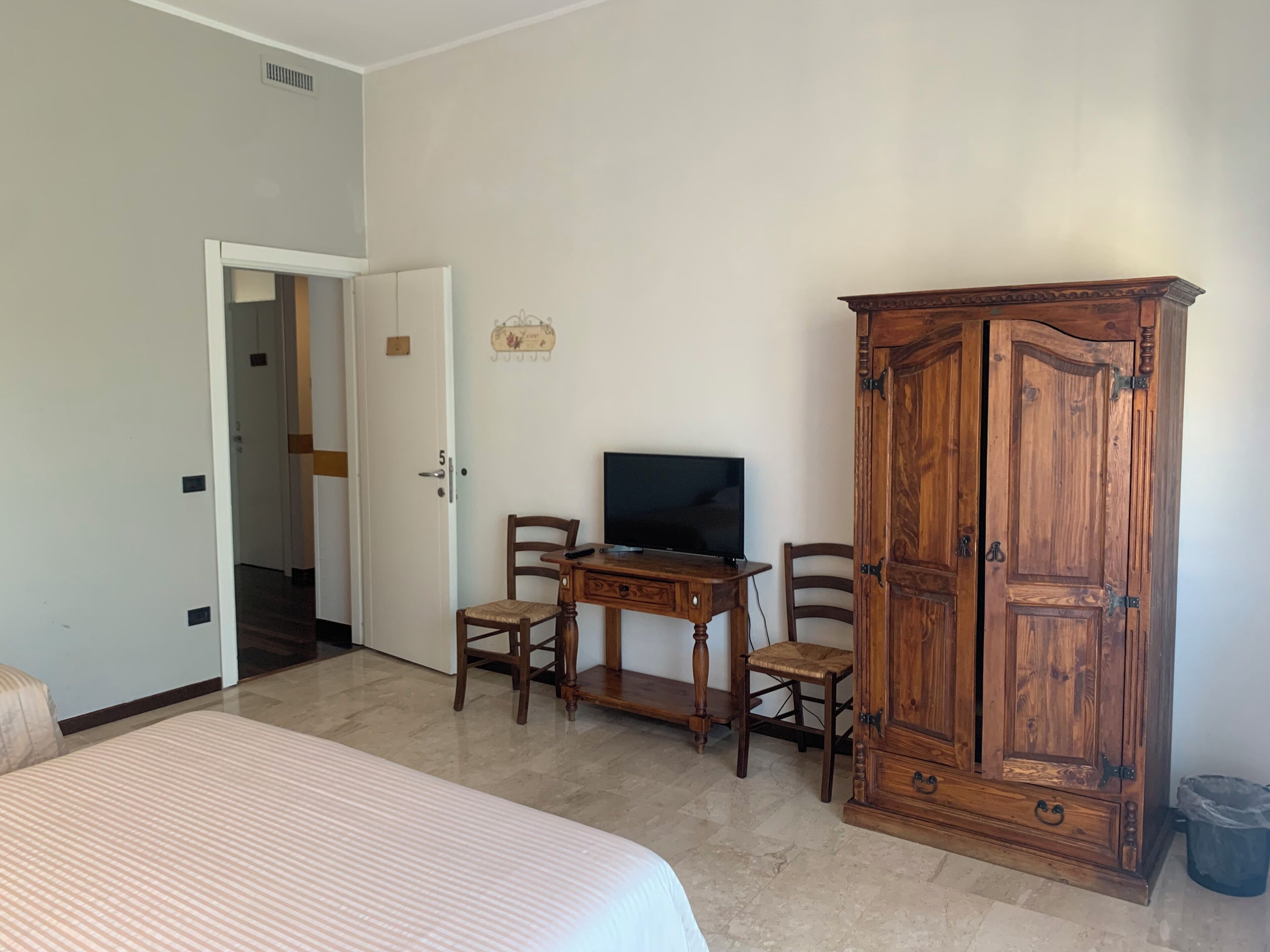 Una habitación con una cama, un armario de madera, un escritorio con televisor y una silla.