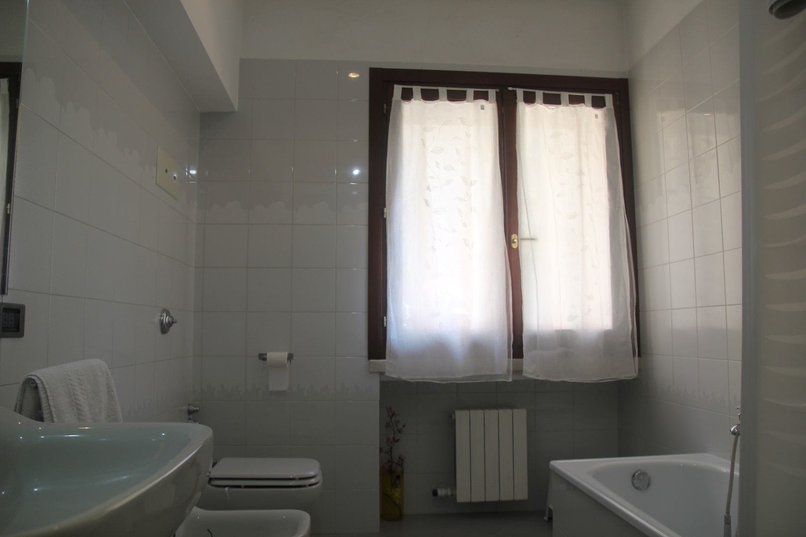 Un bagno con il water, un lavandino, una vasca e una finestra con tende.