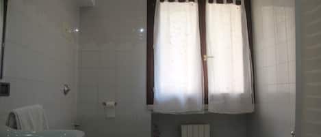Un bagno con il water, un lavandino, una vasca e una finestra con tende.