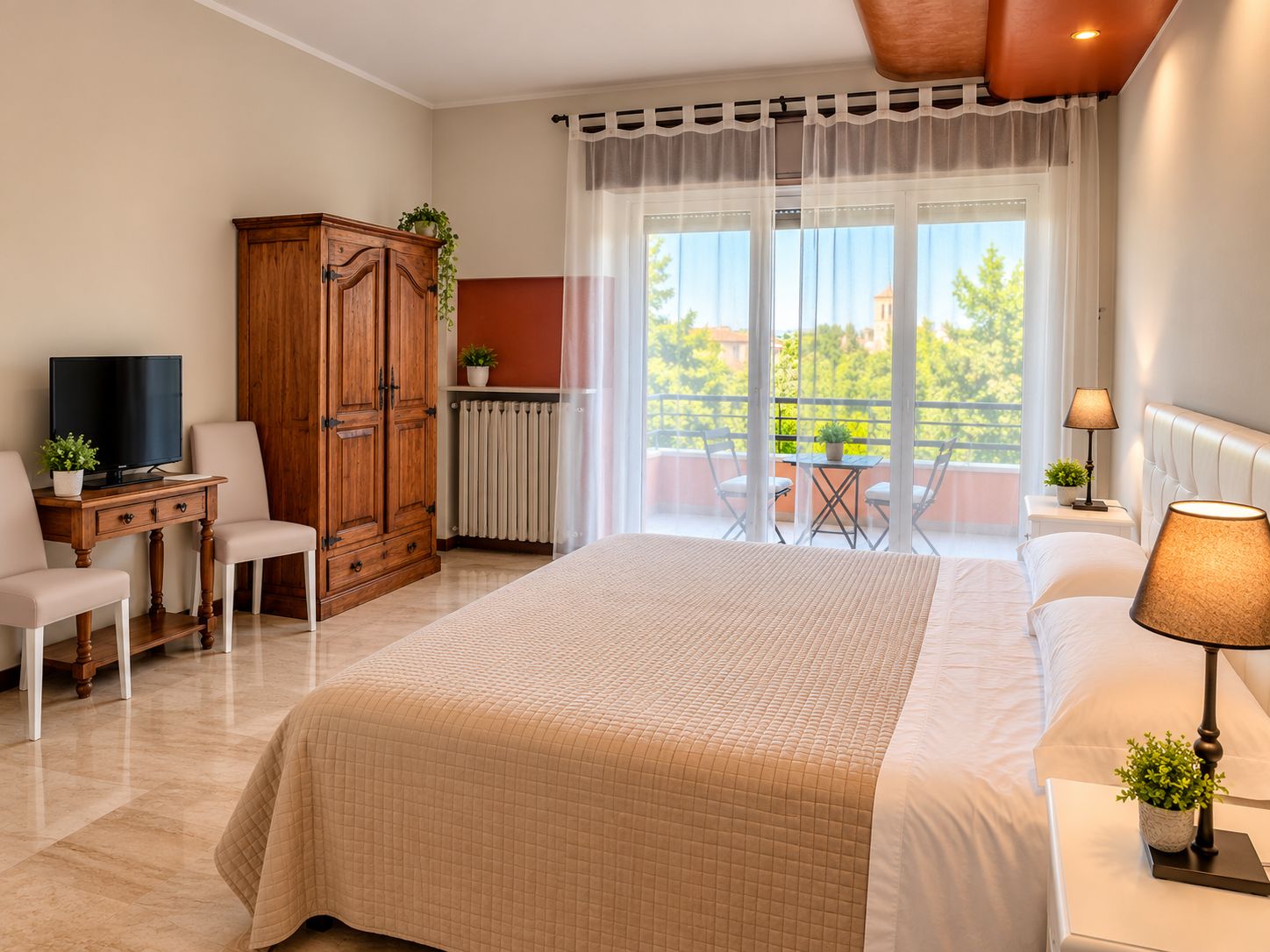 Habitación de hotel con cama, escritorio con televisor, armario, balcón con sillas y vista a zonas verdes.
