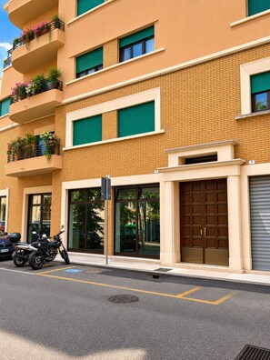 Un edificio de varios pisos con fachada de ladrillo, ventanas amplias y balcones con macetas de flores.