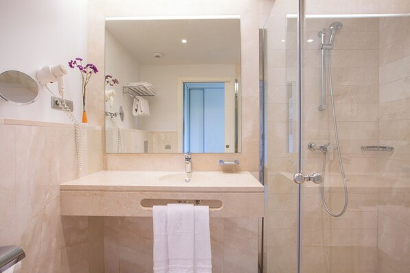 A modern bathroom with a beige marble sink, a glass-enclosed shower, and a blue door in the background.
