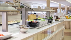 Zona de bufé con diversas opciones de comida, incluyendo sushi y ensaladas, en un hotel moderno.