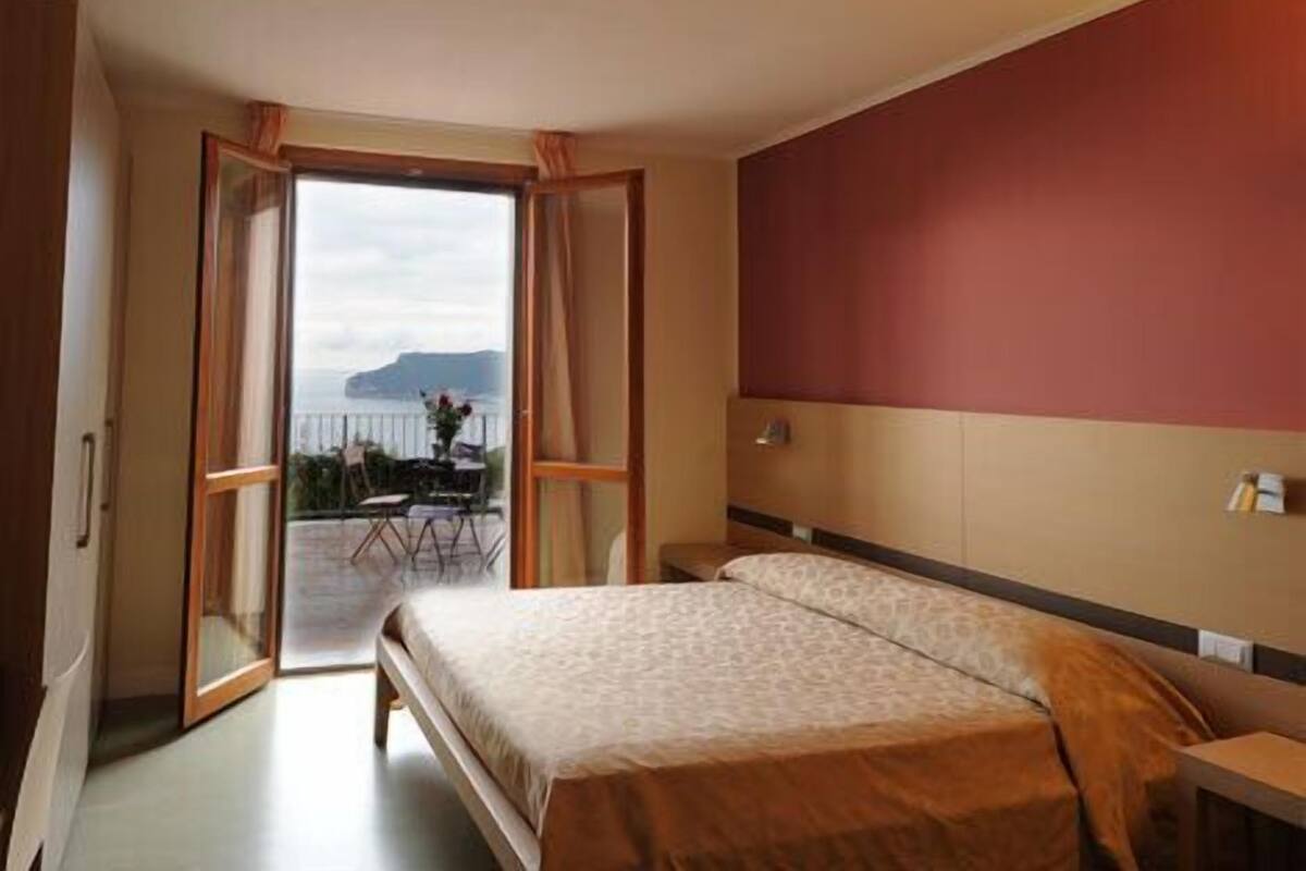 Ein Schlafzimmer mit Bett, Holz-Kopfteil, Meerblick und einem Balkon mit Tisch und Stühlen.