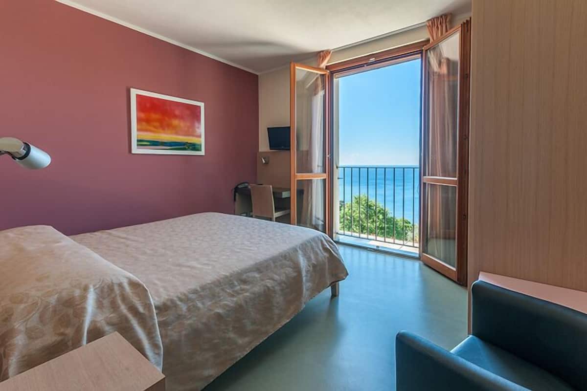 Ein Zimmer mit Bett, Schreibtisch, Stuhl und einem Balkon mit Blick.