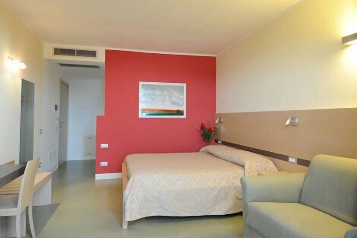 Ein Hotelzimmer mit Bett, Sofa, Schreibtisch und einem Gemälde an der Wand.