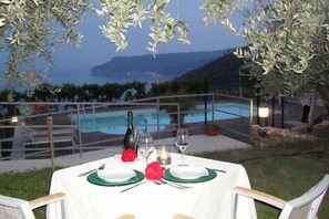 An outdoor dining area with a table set for two, overlooking a pool and a mountainous landscape. - Hotel Oroverde (Bergeggi)
