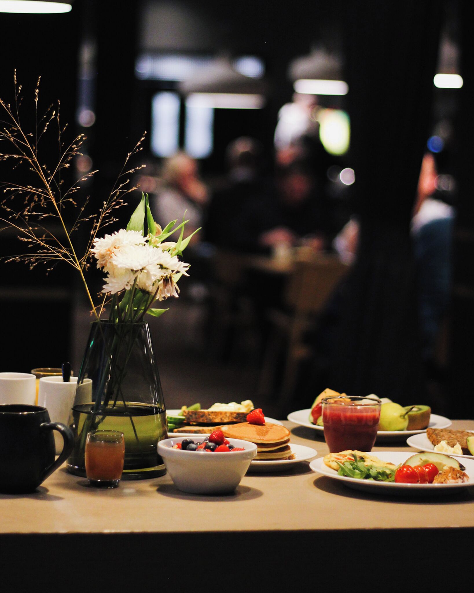 A dining table with various dishes, a vase with flowers, and a glass of juice.