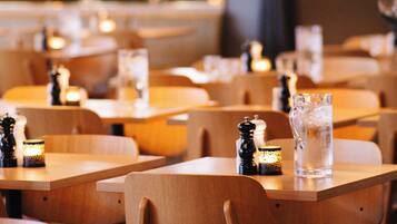 A restaurant interior with wooden tables and chairs, pendant lighting, and a glass pitcher on the tables.