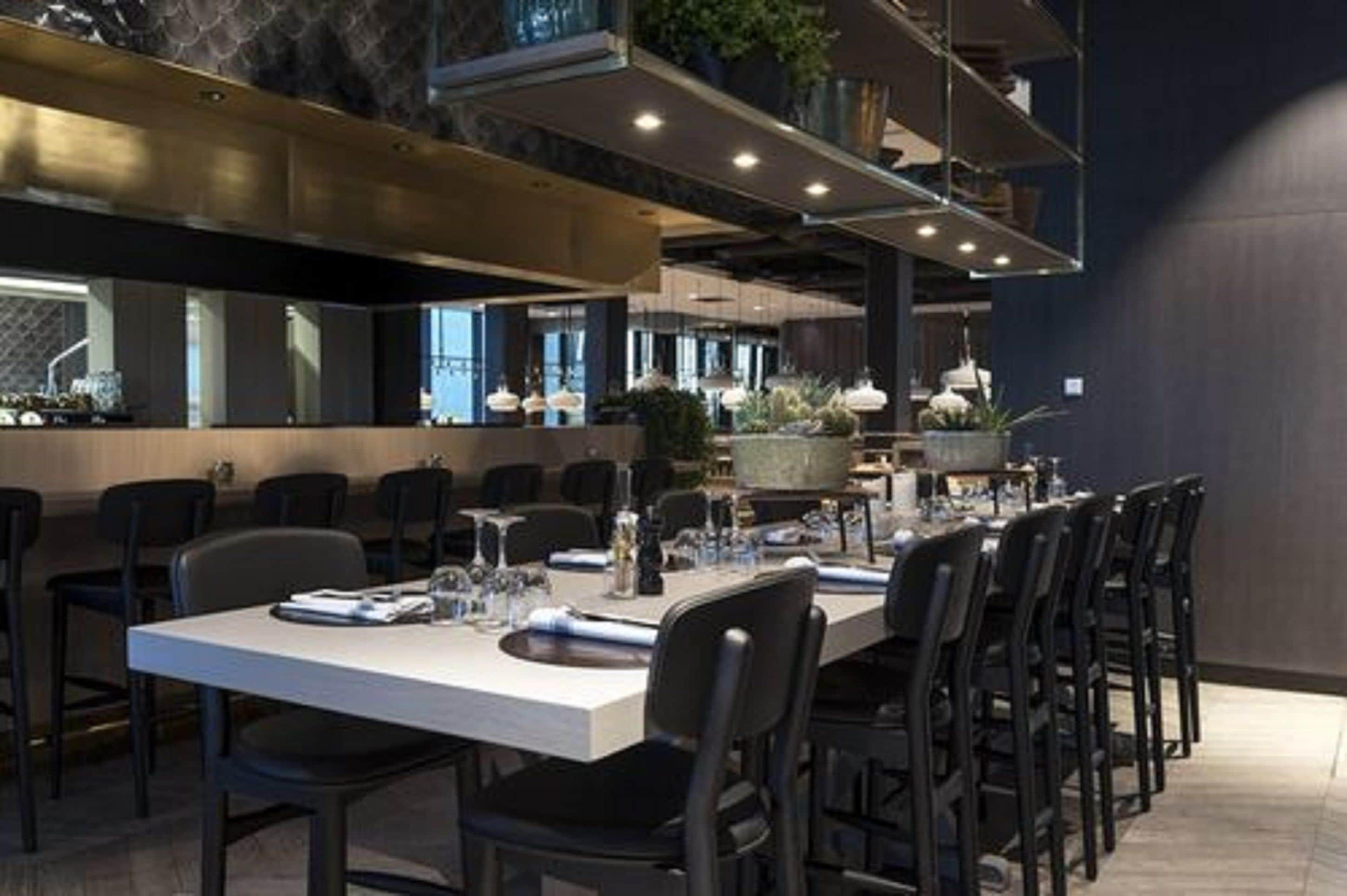 A modern dining area with a long table set for a meal, surrounded by chairs.