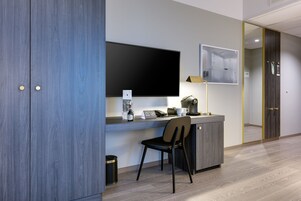 Una habitación de hotel moderna con un escritorio de madera, un televisor de pantalla plana, una silla y una cafetera.