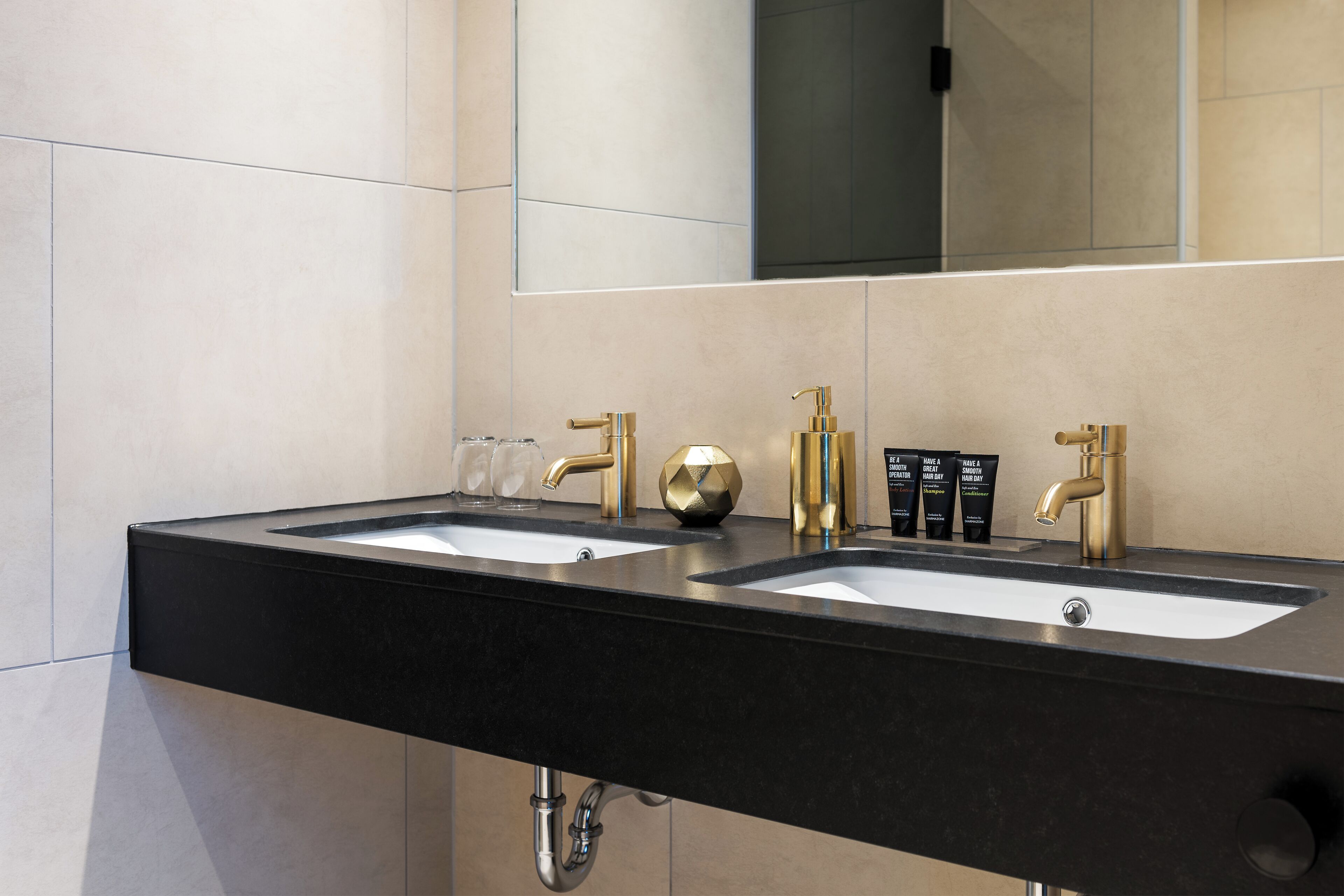 Une salle de bain moderne avec deux vasques, des robinets dorés et un grand miroir.
