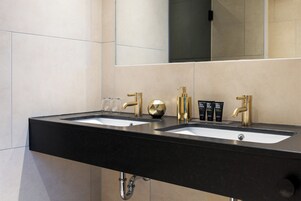 Un baño moderno con dos lavamanos, grifos dorados y un espejo grande.