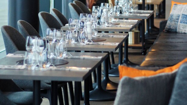 A restaurant with long tables, chairs, hanging pendant lights, and shelves with decorative items. - Clarion Hotel Air (Sola)