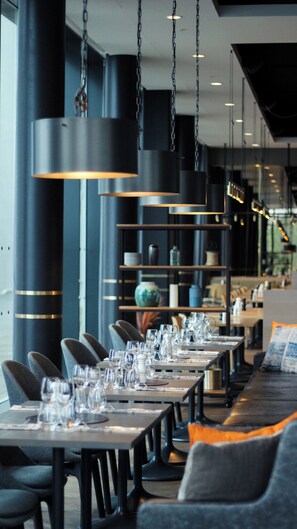 Un restaurant avec de longues tables, des chaises, des lampes suspendues et des étagères ornées d’objets décoratifs.