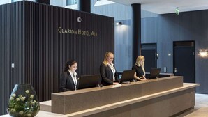 A reception desk at Clarion Hotel Air with three staff members, a modern design, and a large vase of flowers. - Clarion Hotel Air (Sola)