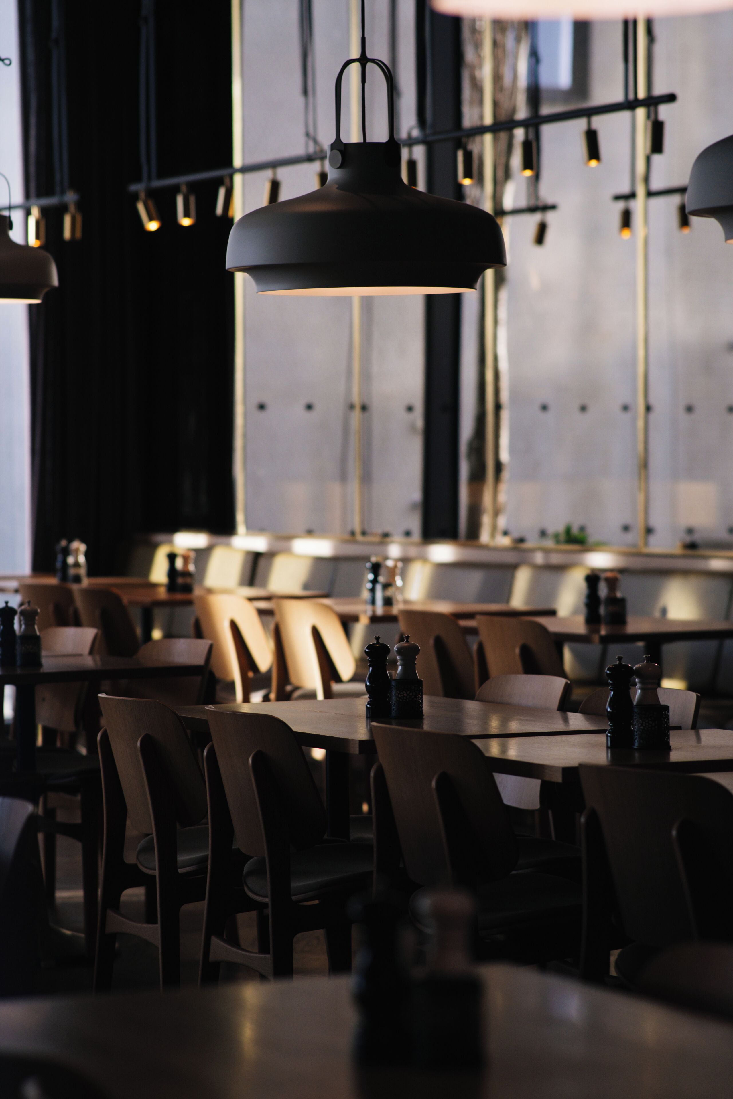 Ein Restaurantinneres mit Tischen, Stühlen, Pendelleuchten und einem großen Fenster.