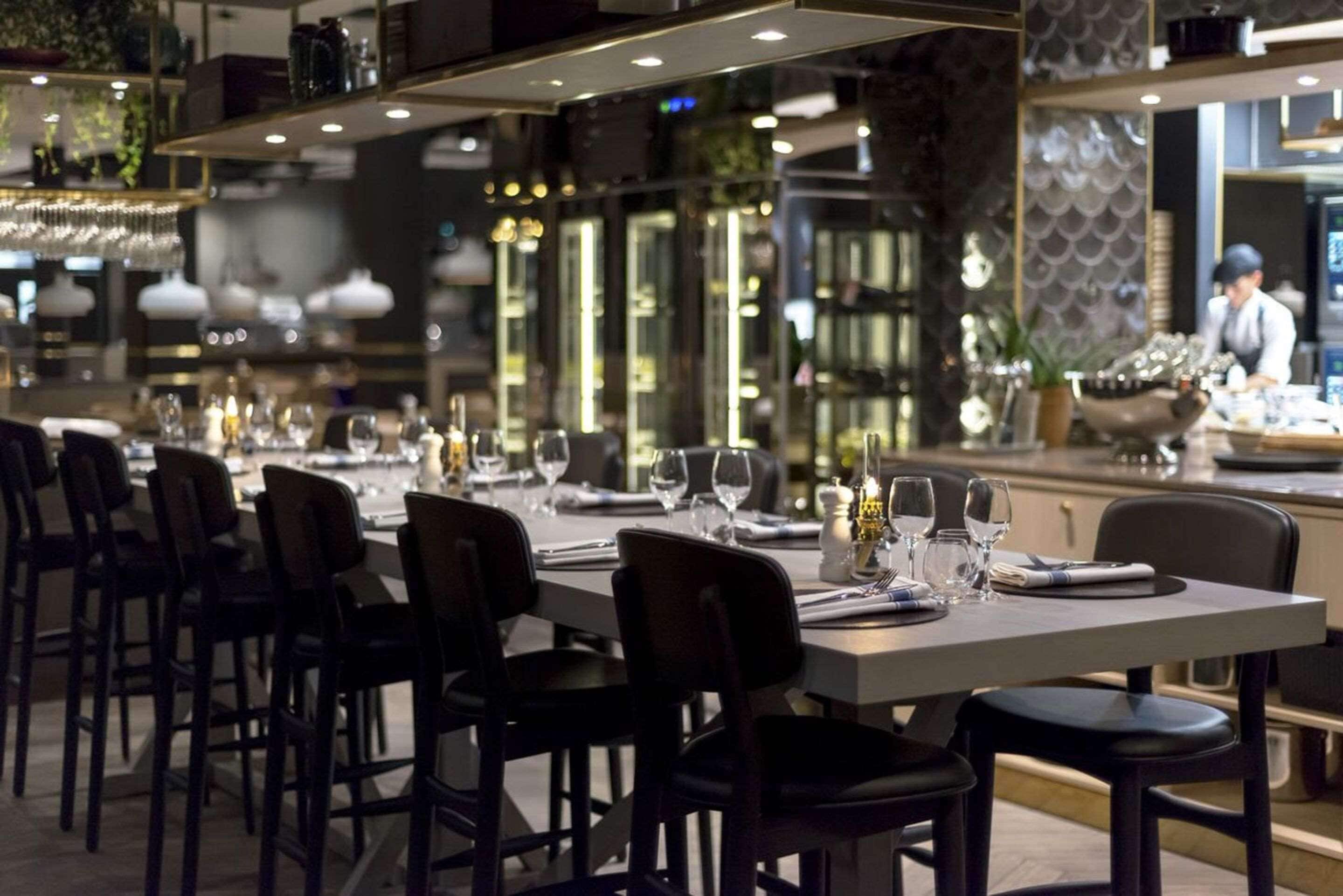 A restaurant with a long table set for dining, chairs, and a bar area in the background.