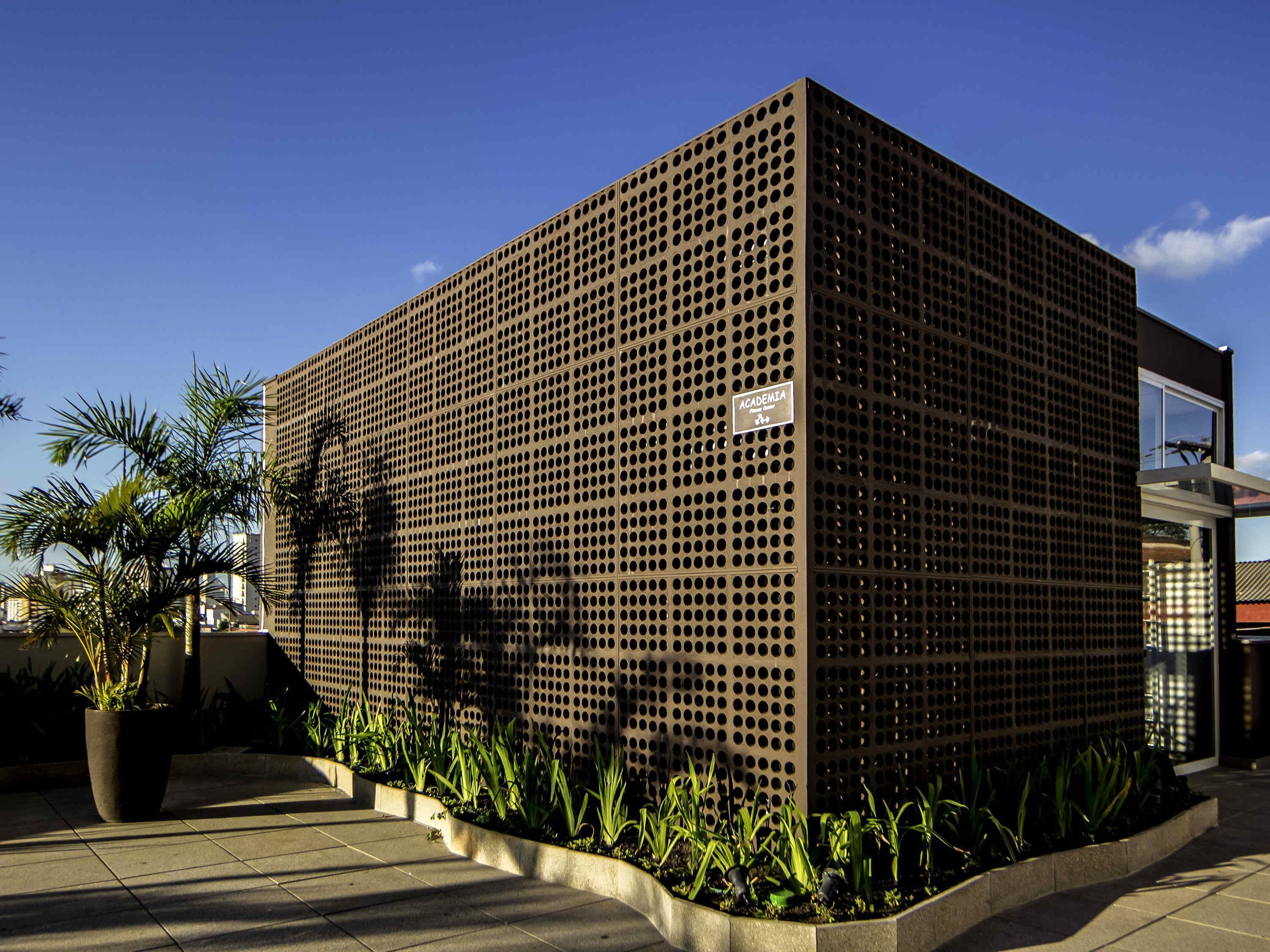 A modern building with a perforated metal facade, a sign indicating 'Academia,' and a landscaped area with plants.
