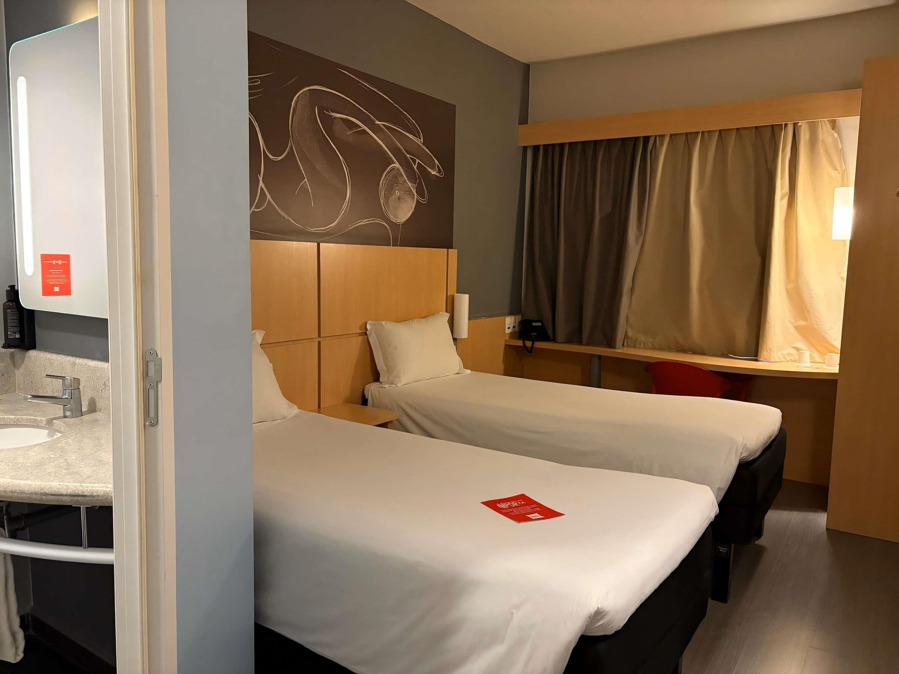 Habitación de hotel con dos camas, un baño con lavamanos y un espejo grande.