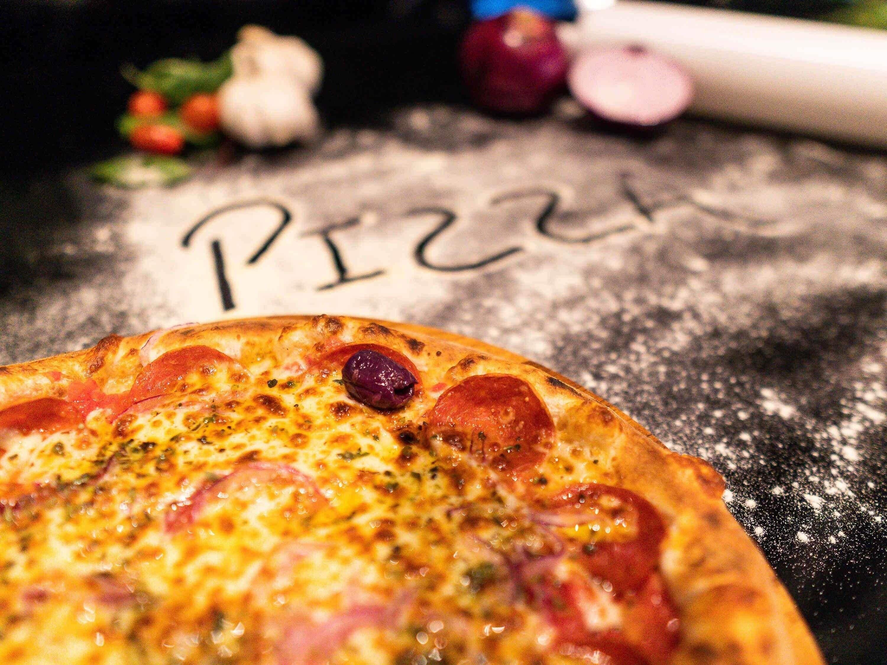 A pizza with pepperoni and a rolling pin in the background.