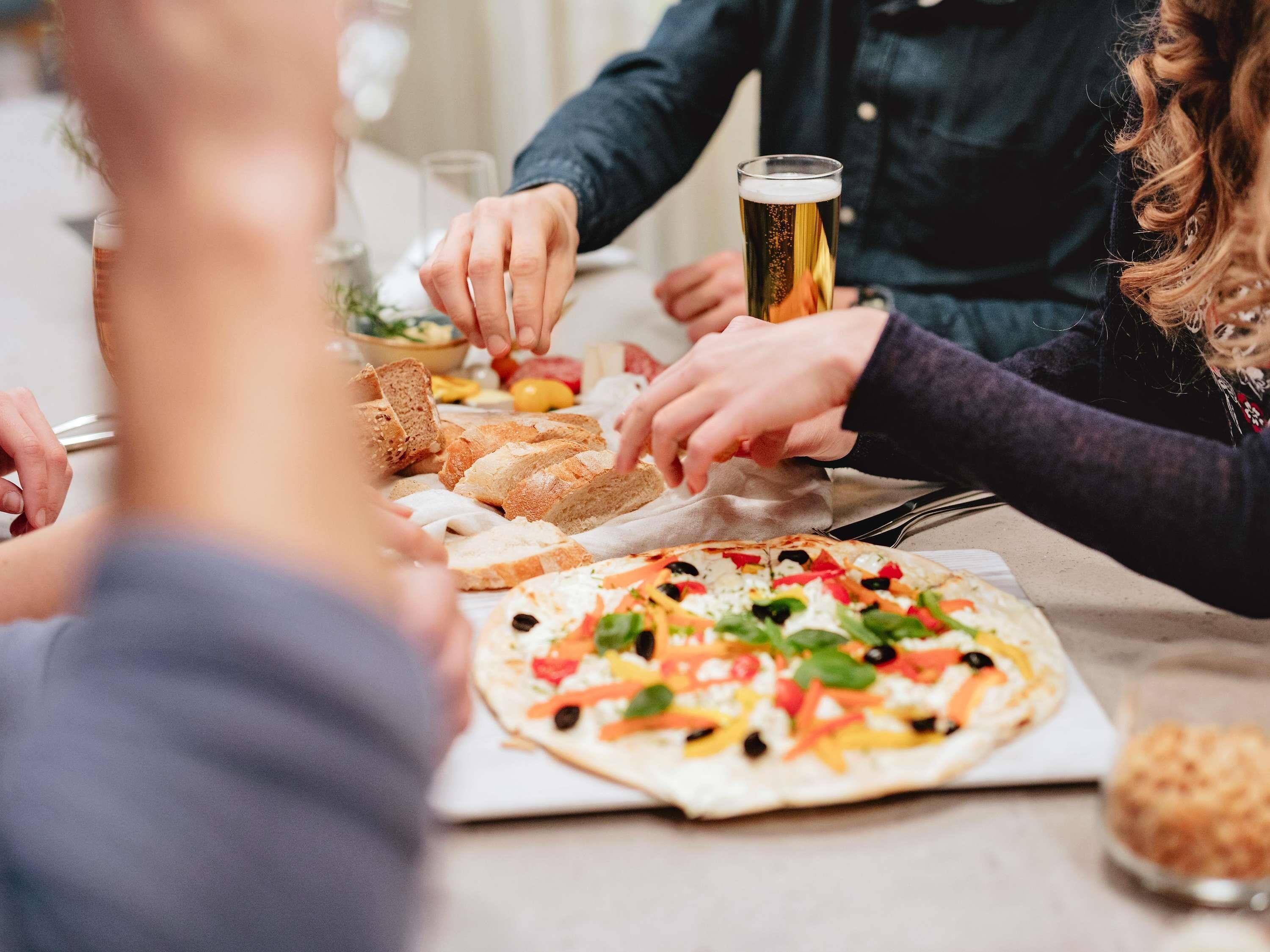 A group of people dining together with a pizza and a glass of beer on the table.