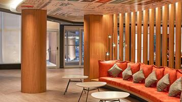 A lobby with a curved orange sofa, two small round tables, and a wooden partition with vertical slats.