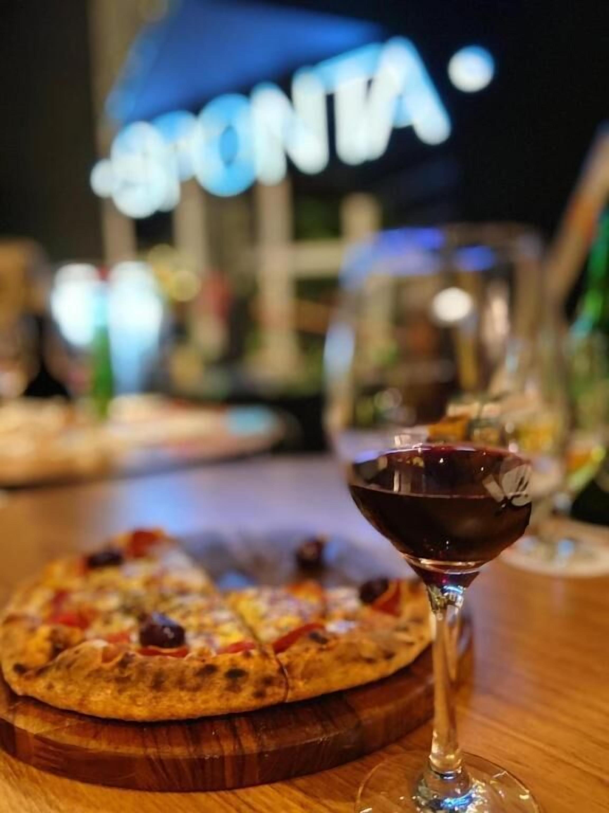 Une table en bois avec une pizza et un verre de vin rouge.