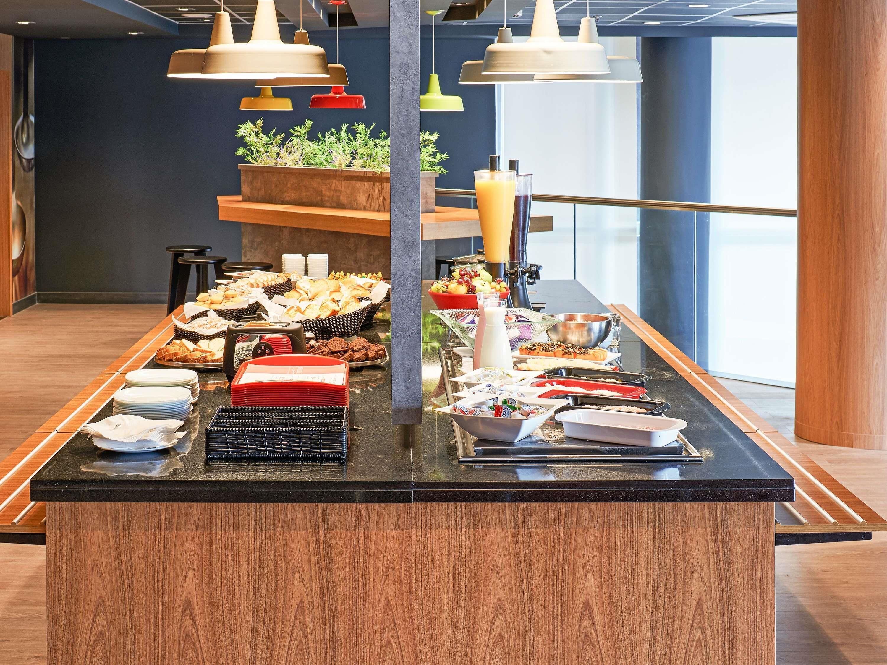 Una mesa de buffet con diversos alimentos y bebidas, incluyendo frutas, pasteles y un dispensador de leche.