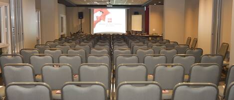 A conference room with rows of grey chairs, a large screen at the front, and a projector.