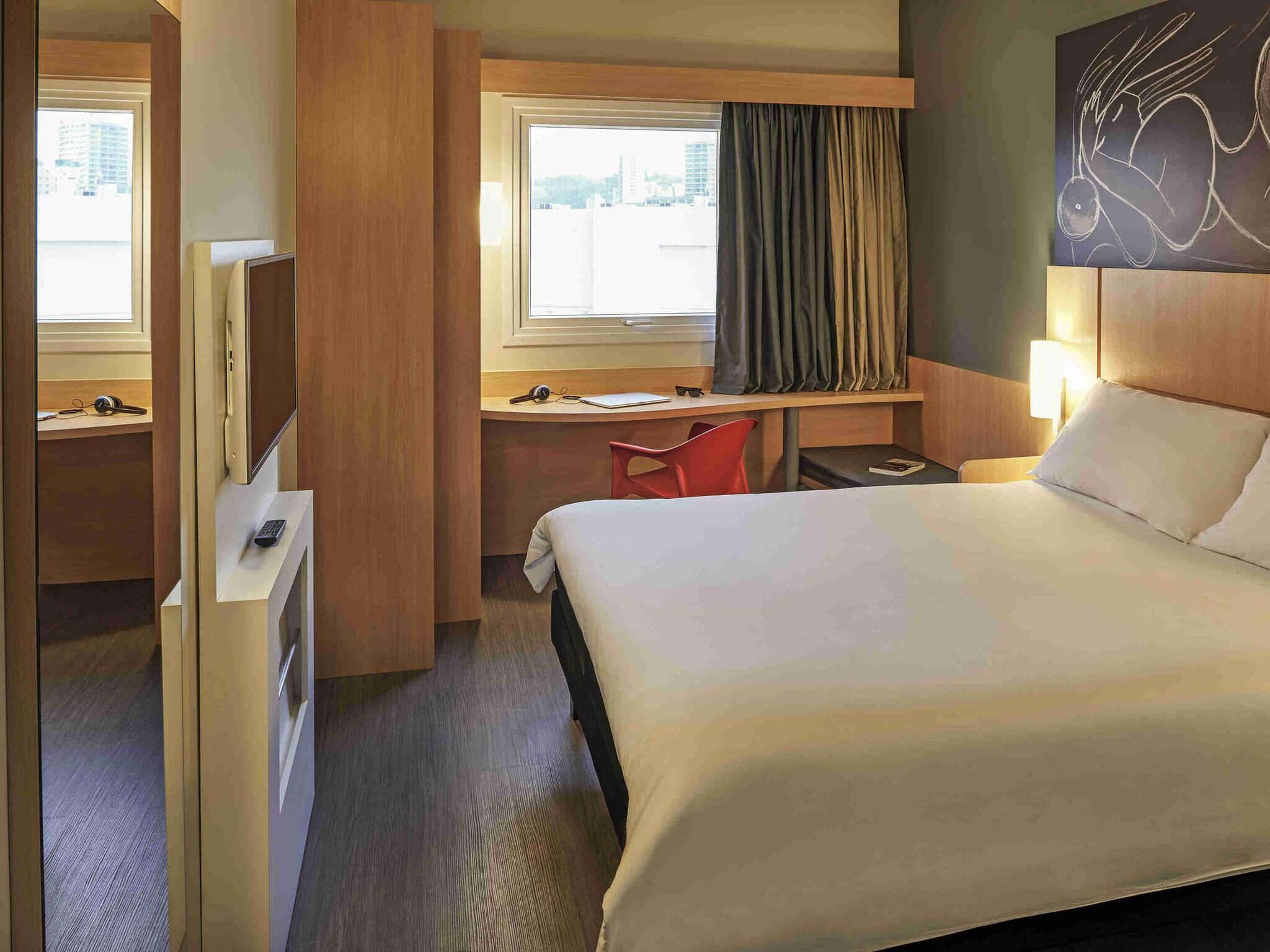 Une chambre d’hôtel avec un lit, un bureau, une chaise et une fenêtre avec des rideaux.