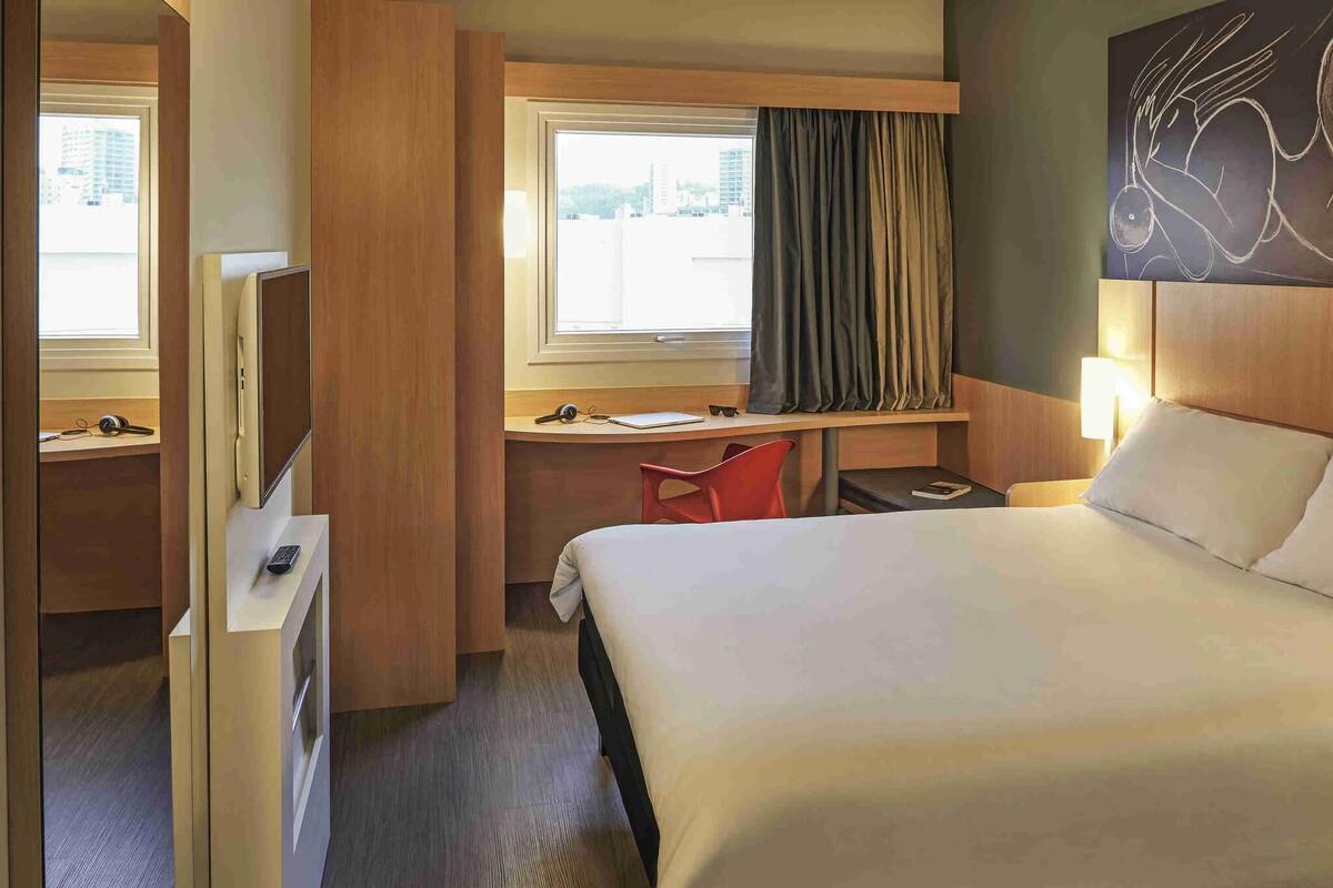 A hotel room with a bed, desk, chair, and a window with curtains.