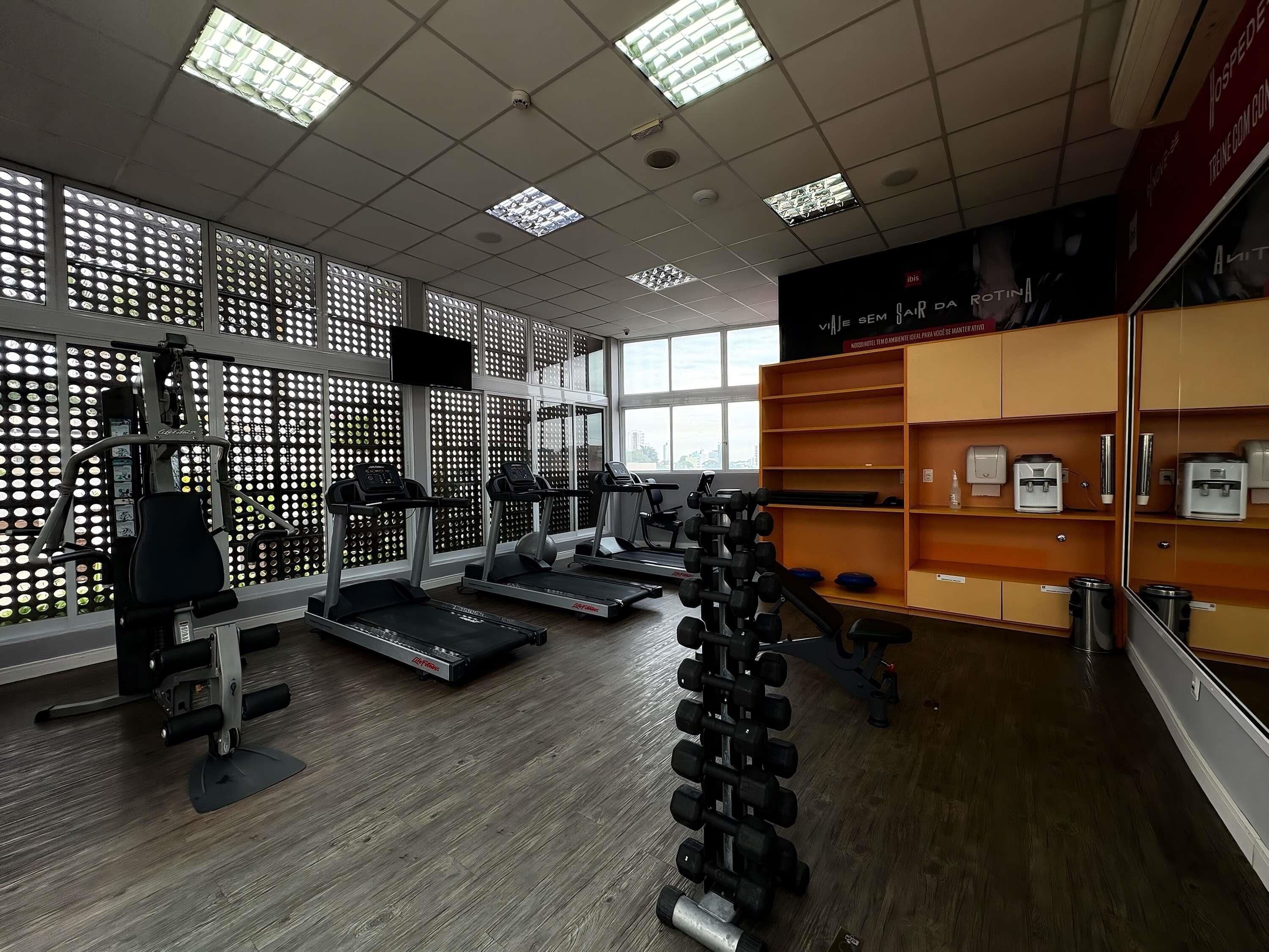 Un gimnasio con cintas de correr, máquinas de pesas y un estante lleno de mancuernas.