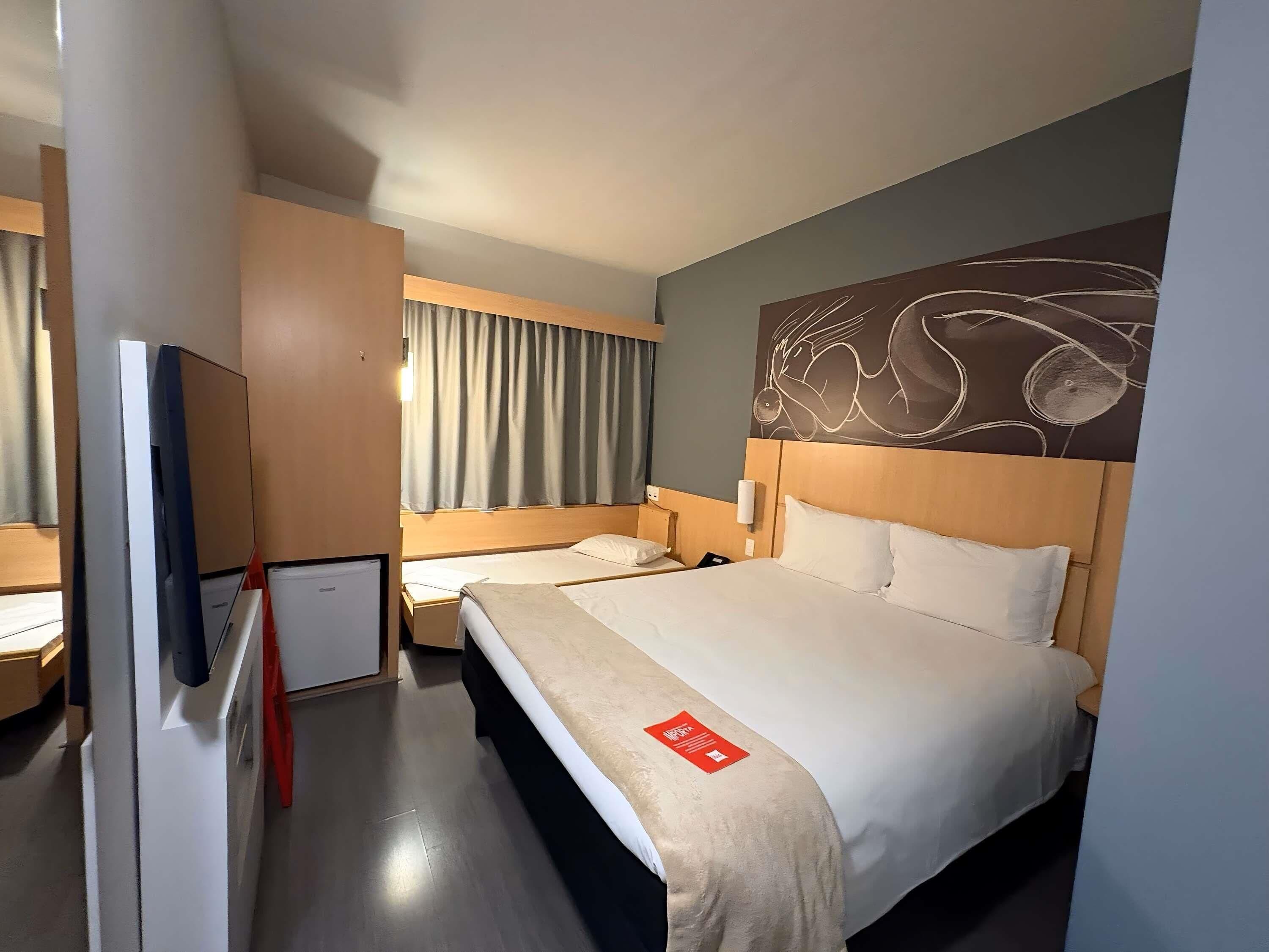 Una habitación de hotel con una cama grande, una cama más pequeña, un escritorio y un televisor.