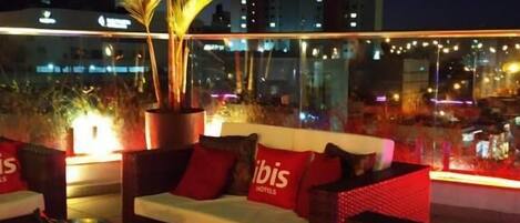 A rooftop lounge area with seating and a potted plant.