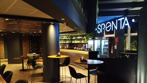 A modern cafe interior with round tables and black chairs, a counter with a neon sign, and a brick wall in the background. - Ibis Jundiai Shopping (Jundiai)
