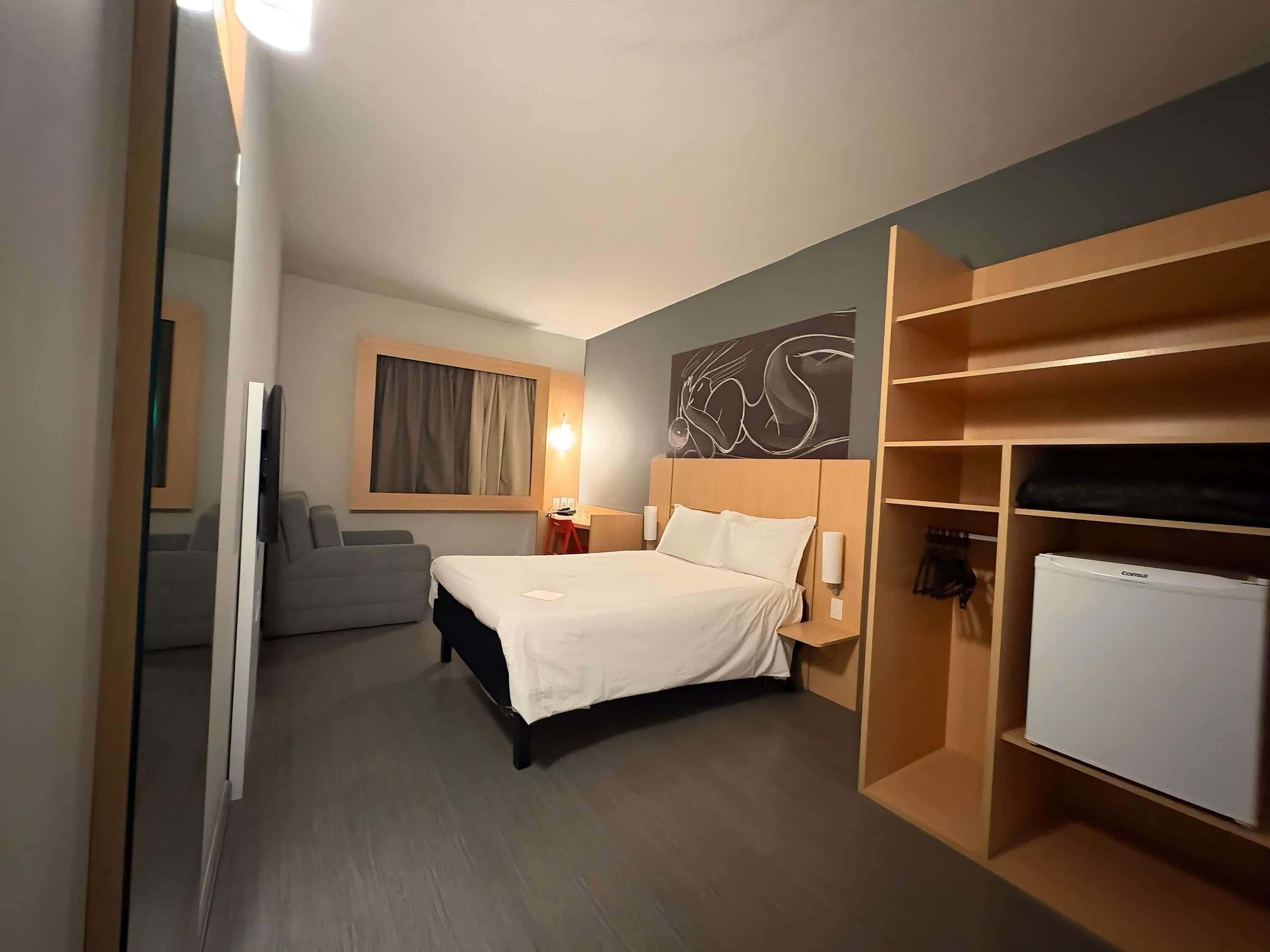 Ein Hotelzimmer mit einem Bett, einem Schreibtisch, einem Stuhl, einem Kleiderschrank und einem Fernseher.