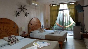 Habitación de hotel con dos camas, cabecera de madera, decoración con estrella de mar, una hamaca y un televisor sobre un soporte.