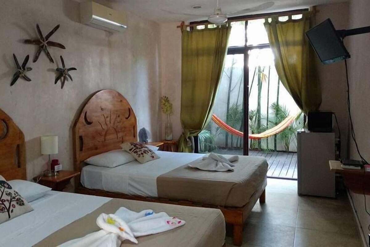 A hotel room with two beds, a wooden headboard, a starfish decoration, a hammock, and a TV on a stand.