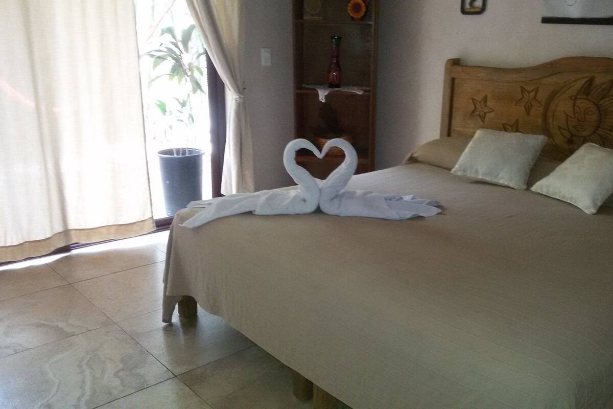 A hotel room with a bed, a wooden headboard, and a window with curtains.