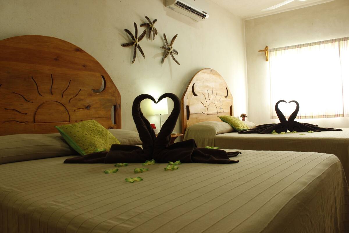 A hotel room with two beds, each with a unique wooden headboard design. There are decorative starfish on the wall, and a heart-shaped decoration on one of the beds.