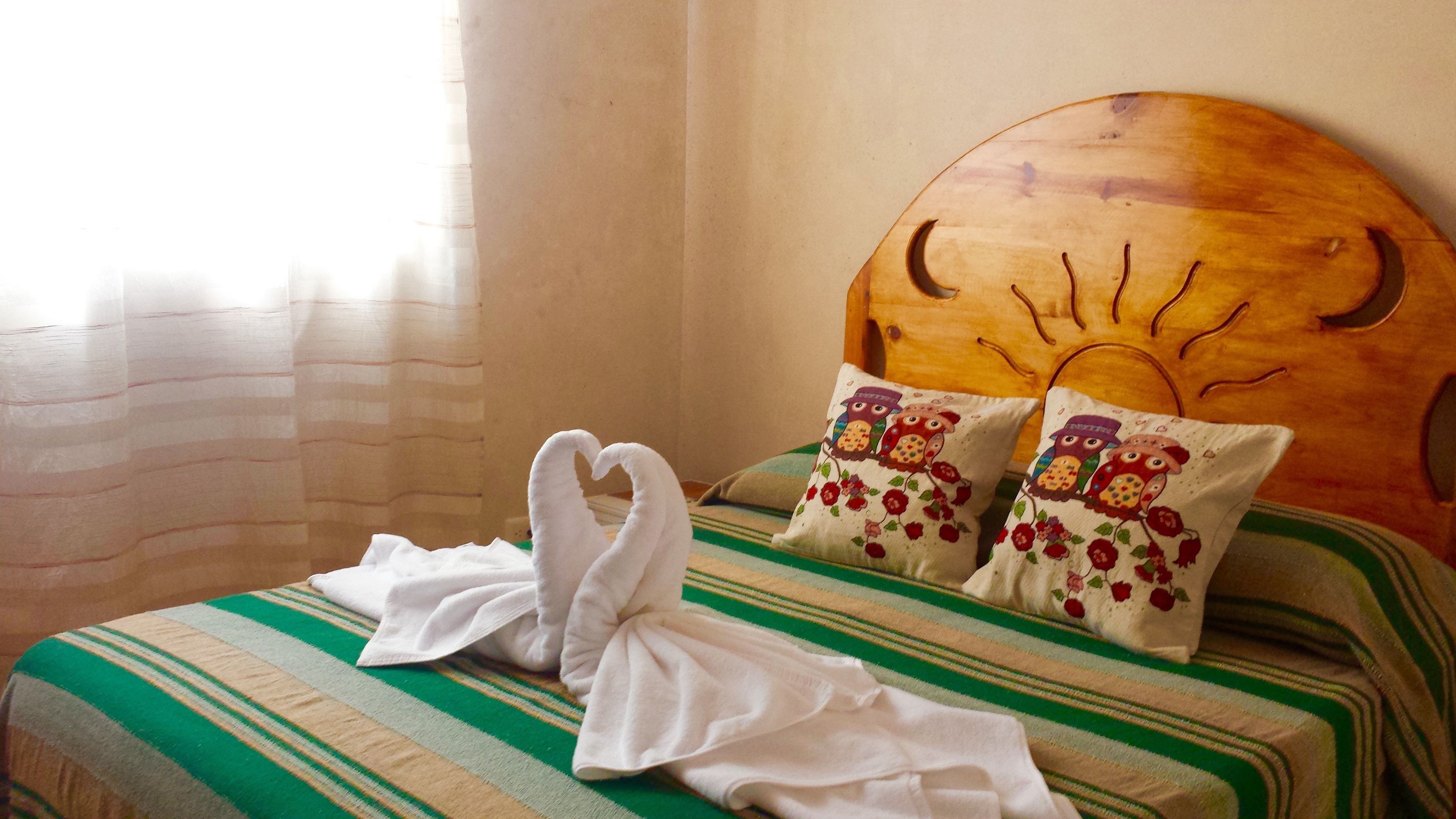 A bed with a striped green and beige bedspread, two pillows with owl designs, and two towels folded on the bed.