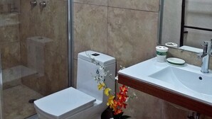 Un baño con cabina de ducha de vidrio, inodoro, lavabo con espejo y un jarrón con flores.