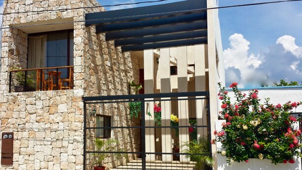 Un edificio de piedra con balcón, entrada porticada y plantas en macetas.